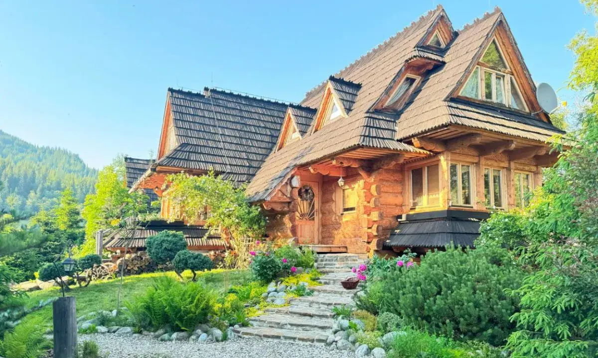 Piękny, drewniany domek w górach z dala od cywilizacji, otoczony zielenią i kwiatami.