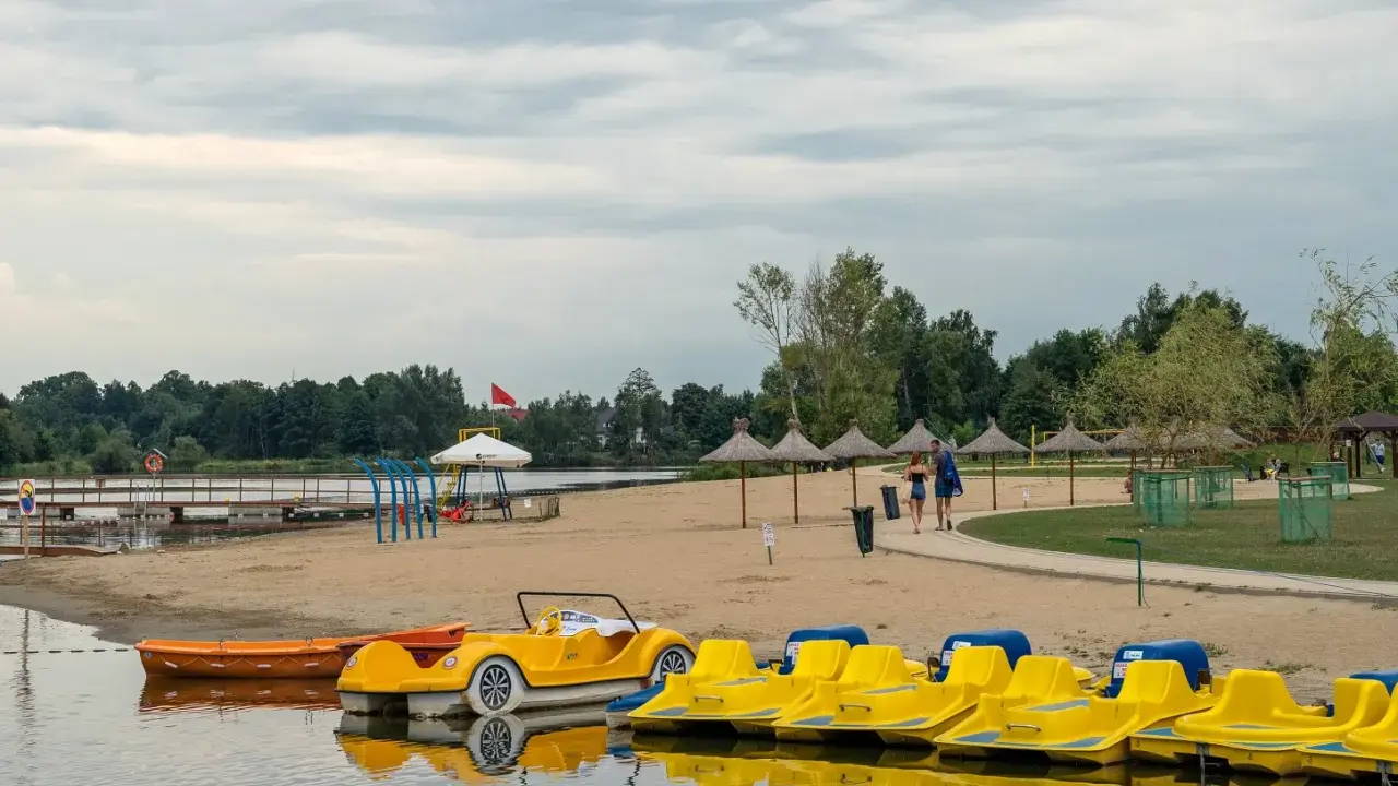 Plaża z żółtymi rowerami wodnymi i łódkami, idealna na weekendowy wypad na Mazury blisko Warszawy.