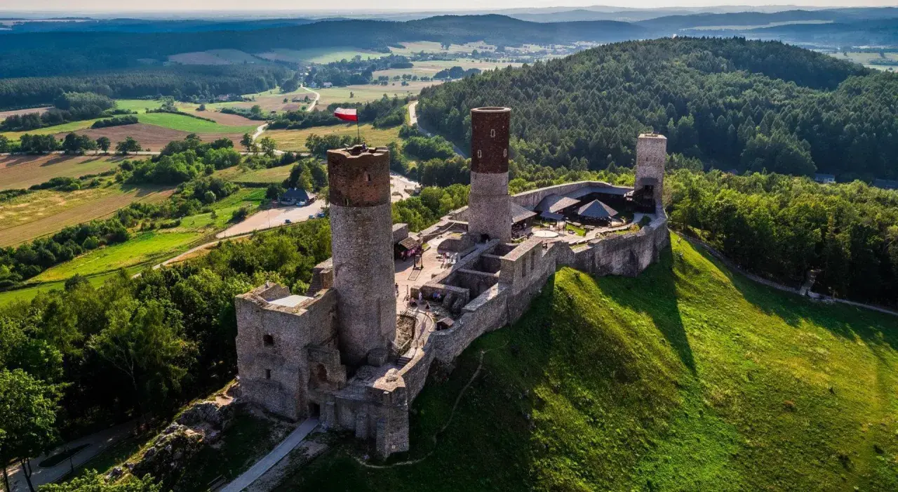 Zamek w Górach Świętokrzyskich, majestatycznie wznoszący się na wzgórzu, otoczony zielenią i malowniczym krajobrazem.