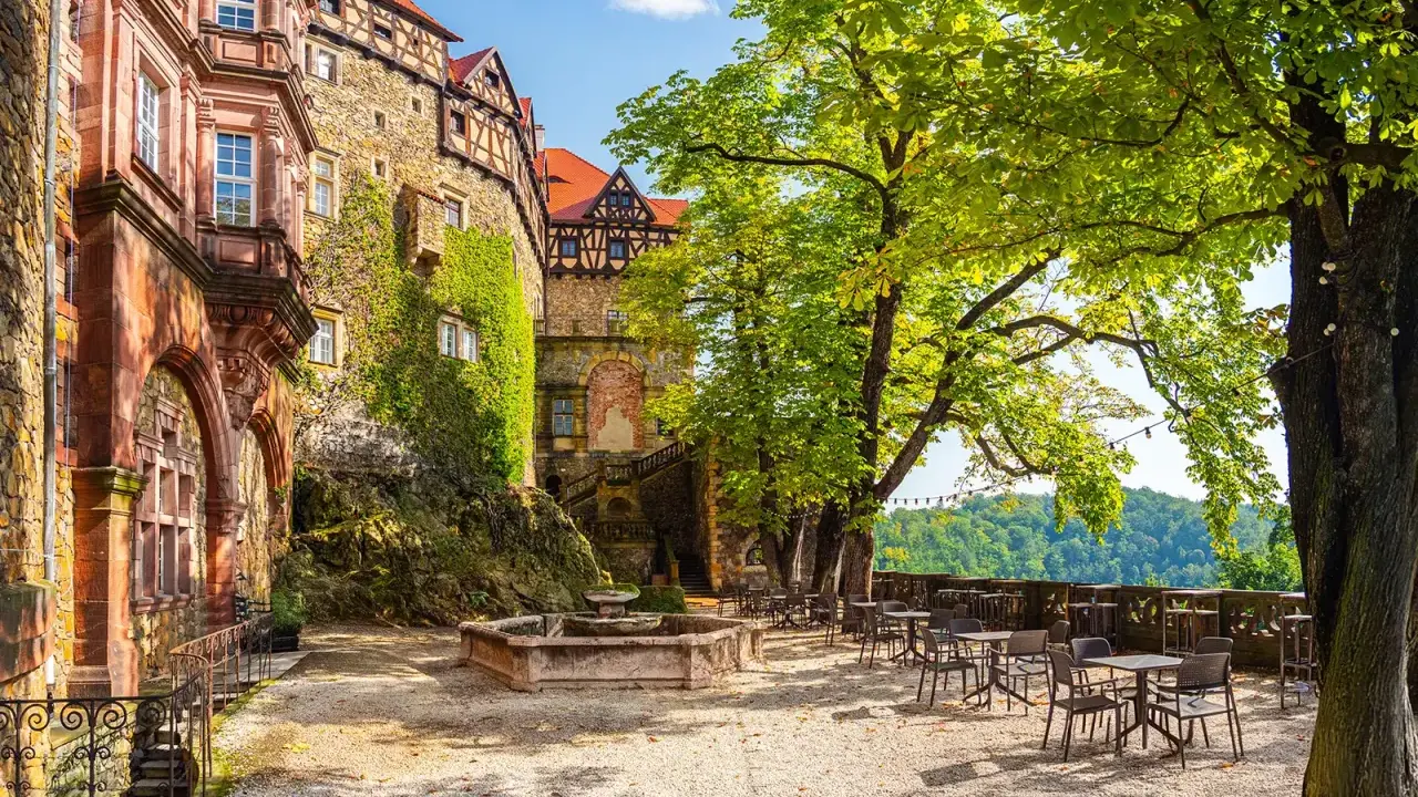 Zamek Książ z tarasami i fontanną, otoczony zielenią, zaprasza do odpoczynku.