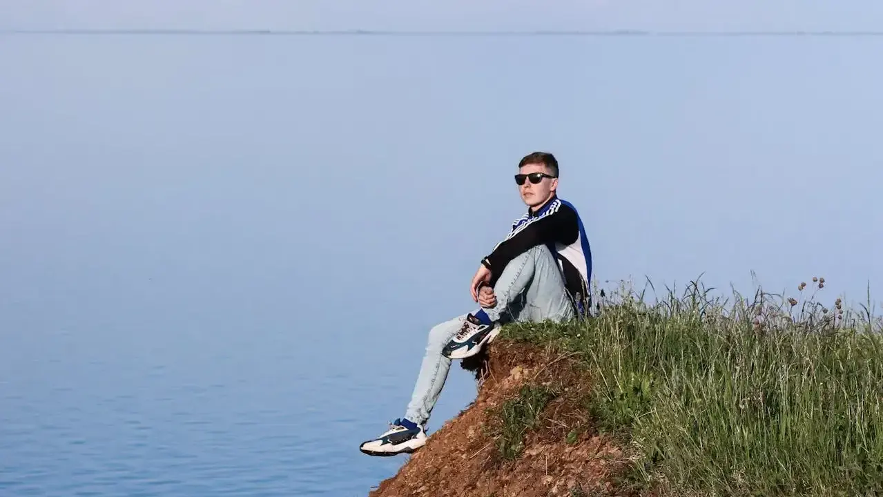 Chłopak siedzi na skarpie nad wodą. Idealne miejsce, gdzie na wakacje z nastolatkiem w Polsce, by poczuć wolność i podziwiać widoki.