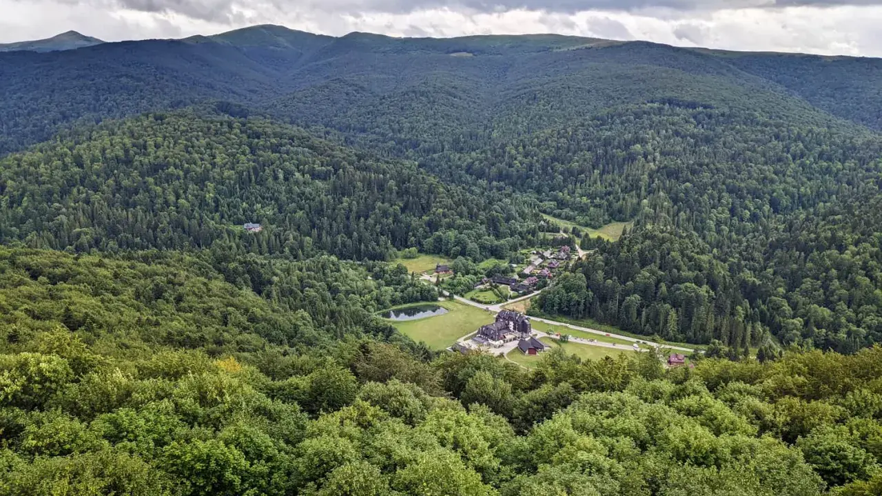 Widok z tarasu widokowego Bieszczady na zieloną dolinę z jeziorem i zabudowaniami.