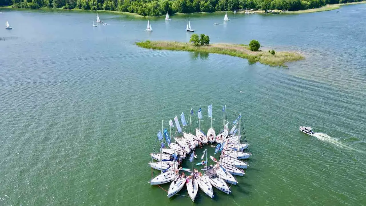 Żaglówki tworzą okrąg na jeziorze, idealne atrakcje Warmia i Mazury. W tle las i mała wyspa.