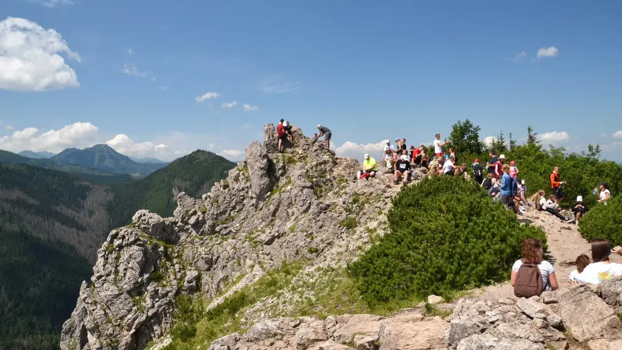 Grupa turystów odpoczywa na skalistym szczycie, podziwiając widok na **Dolinę Białego**.