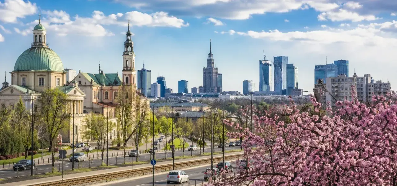 Majówka w Warszawie: zabytkowy kościół i nowoczesne wieżowce na tle kwitnącej wiśni.