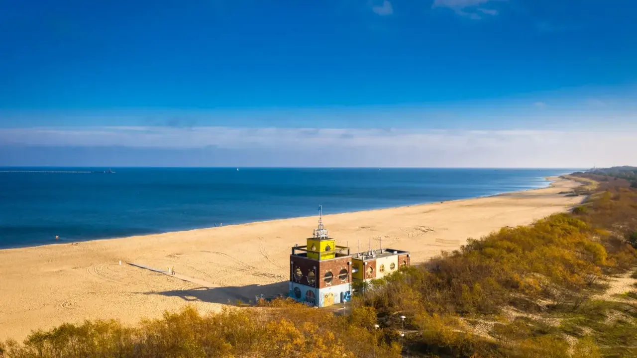 Piękna plaża i morze, idealne na spacer po urokliwych **miejscowościach nad morzem koło Gdańska**. W oddali widać charakterystyczny budynek.
