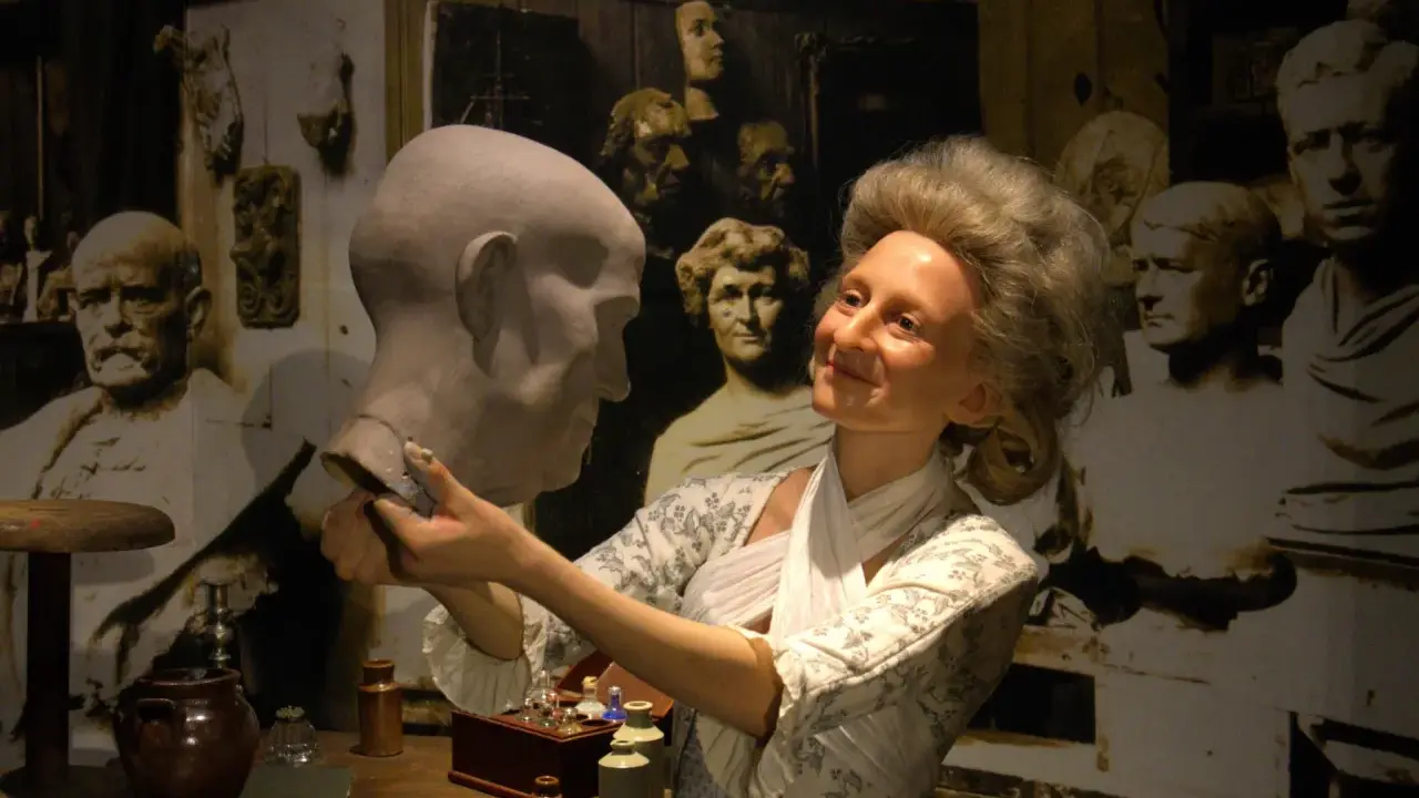 W muzeum figur woskowych artystka w historycznym stroju pracuje nad popiersiem.