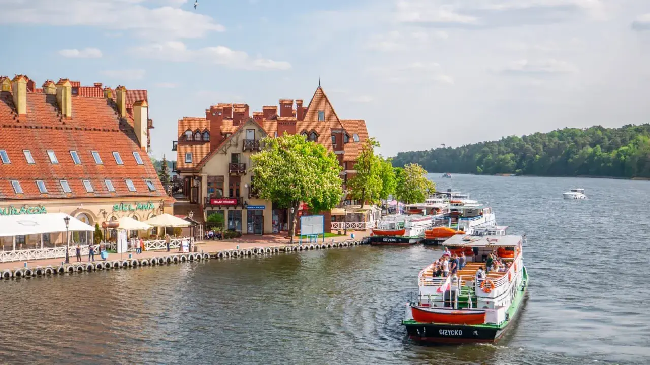 Port w Giżycku, gdzie cumują statki wycieczkowe, to jedna z głównych atrakcji miasta. W tle malownicze kamieniczki i zielone lasy.