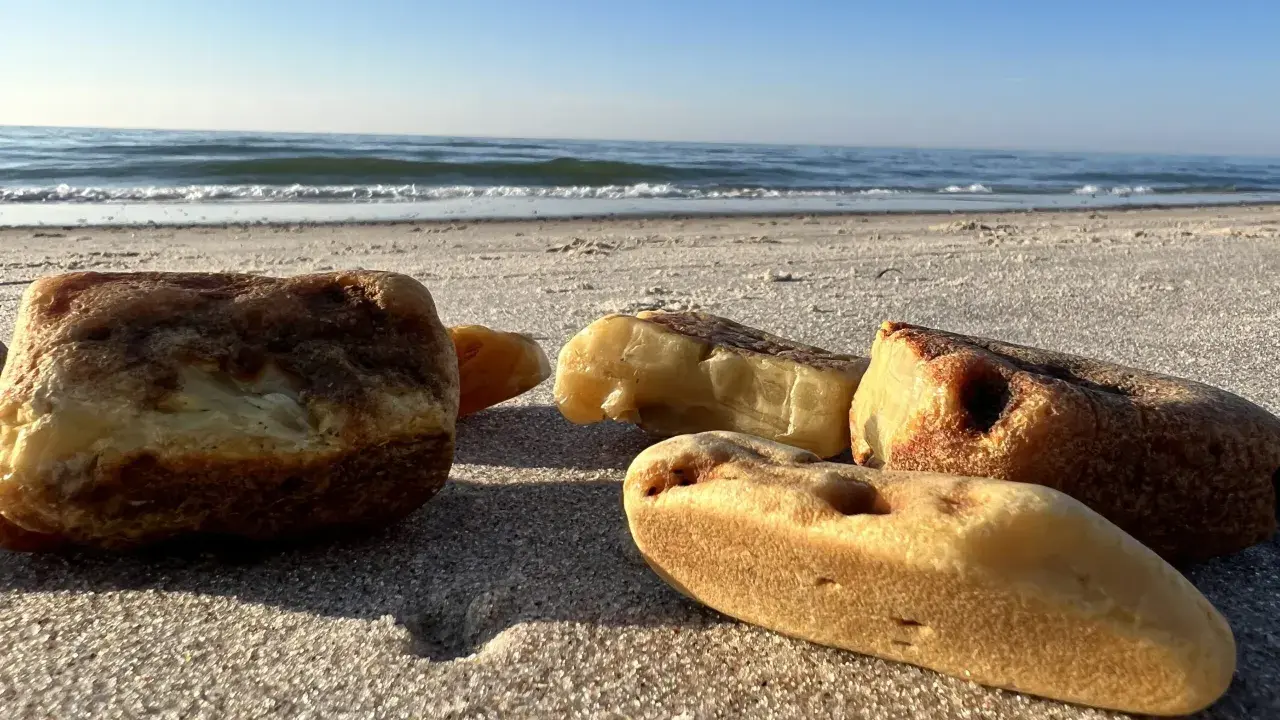 Kilka kawałków bursztynu leży na piaszczystej plaży, w tle widać spokojne morze i błękitne niebo.