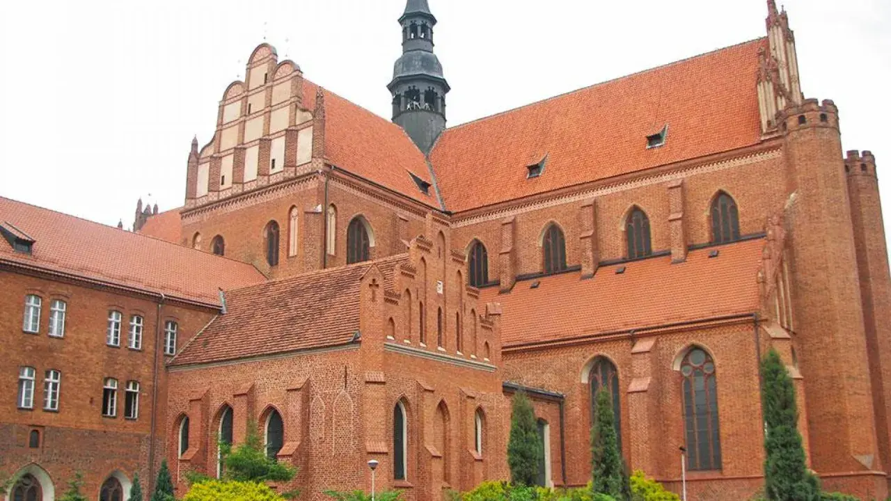 Majestatyczna pelplińska katedra z cegły, z charakterystycznymi dachami i wieżą, góruje nad otoczeniem.