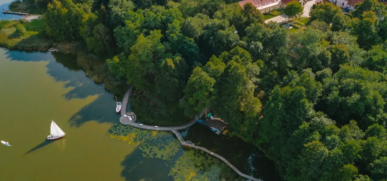 Idealne miejsce, gdzie nad jezioro w Polsce. Drewniana kładka prowadzi do łodzi i żaglówki, otoczone bujną zielenią.