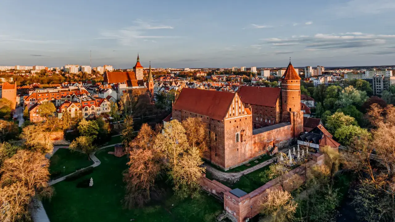 Zachód słońca nad zamkami na Mazurach. Czerwone dachy i ceglane mury w blasku złotej godziny.