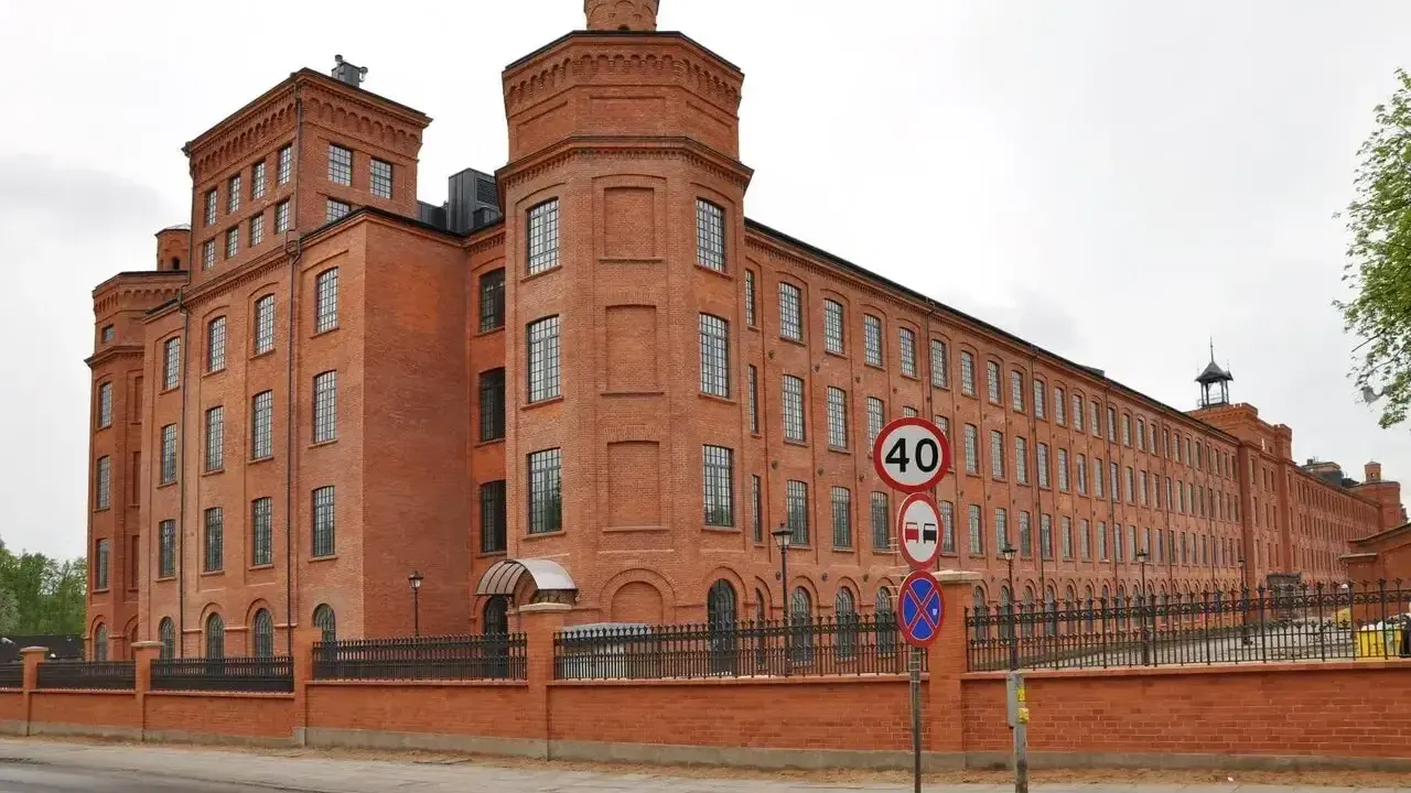 Imponujący ceglany budynek dawnego Księży Młyn, idealny na zwiedzanie. Widać znaki drogowe i ogrodzenie.