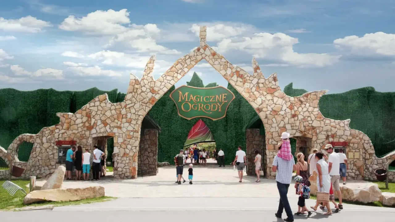 Kamienna brama "Magiczne Ogrody" zaprasza na świetne atrakcje dla nastolatków. Rodziny wchodzą do parku rozrywki.