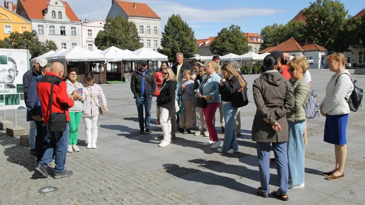 Grupa turystów słucha przewodnika na rynku w Chełmnie, poznając lokalną trasę.