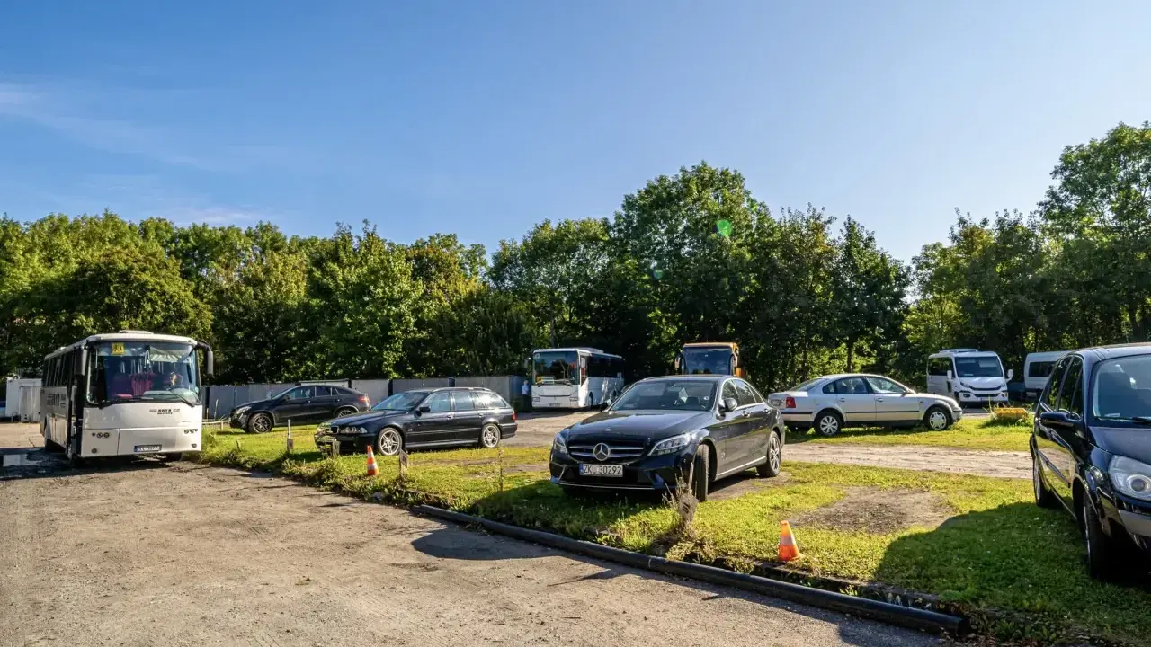 Na parkingu przy zamku Bolków stoi kilka samochodów i autobusów.