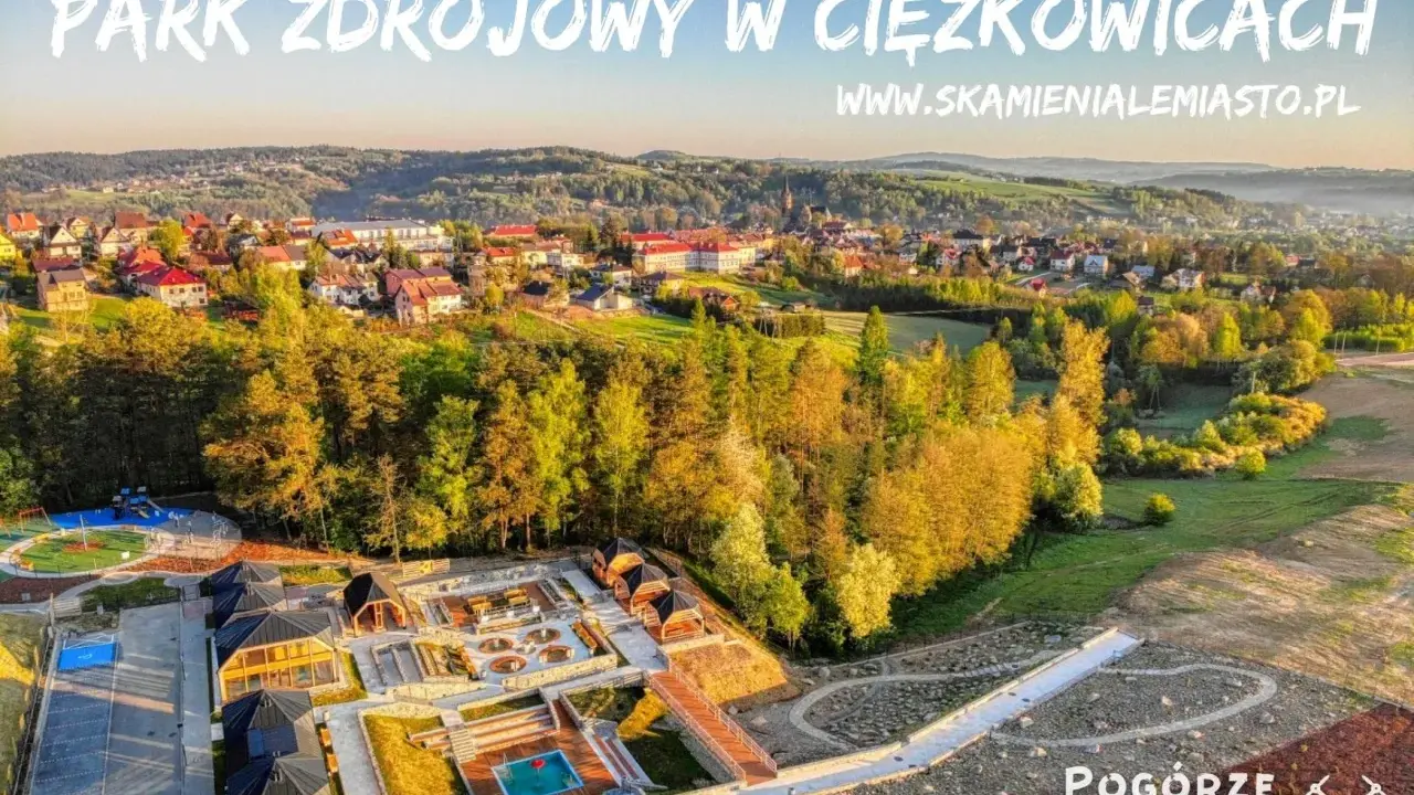 Widok z lotu ptaka na park zdrojowy w Ciężkowicach z placem zabaw, basenem i drewnianymi altanami.