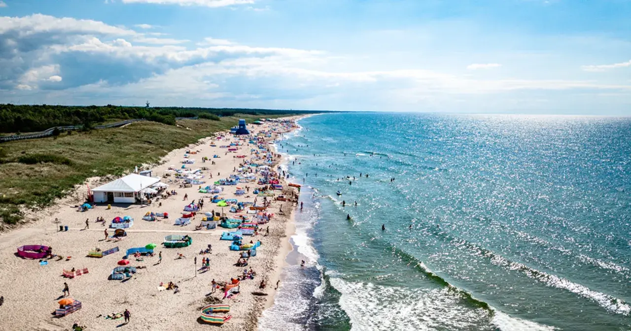 Tłum ludzi na plaży w Darłowie, korzystających z uroków lata. Wiele kolorowych parawanów i namiotów, a w wodzie kąpielowicze. To idealne darłowo atrakcje dla każdego.