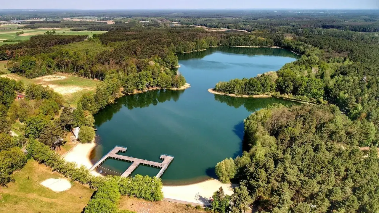 Malownicze jeziora w Zielonej Górze otoczone lasem, z drewnianym pomostem i piaszczystą plażą. Idealne miejsce na wypoczynek.