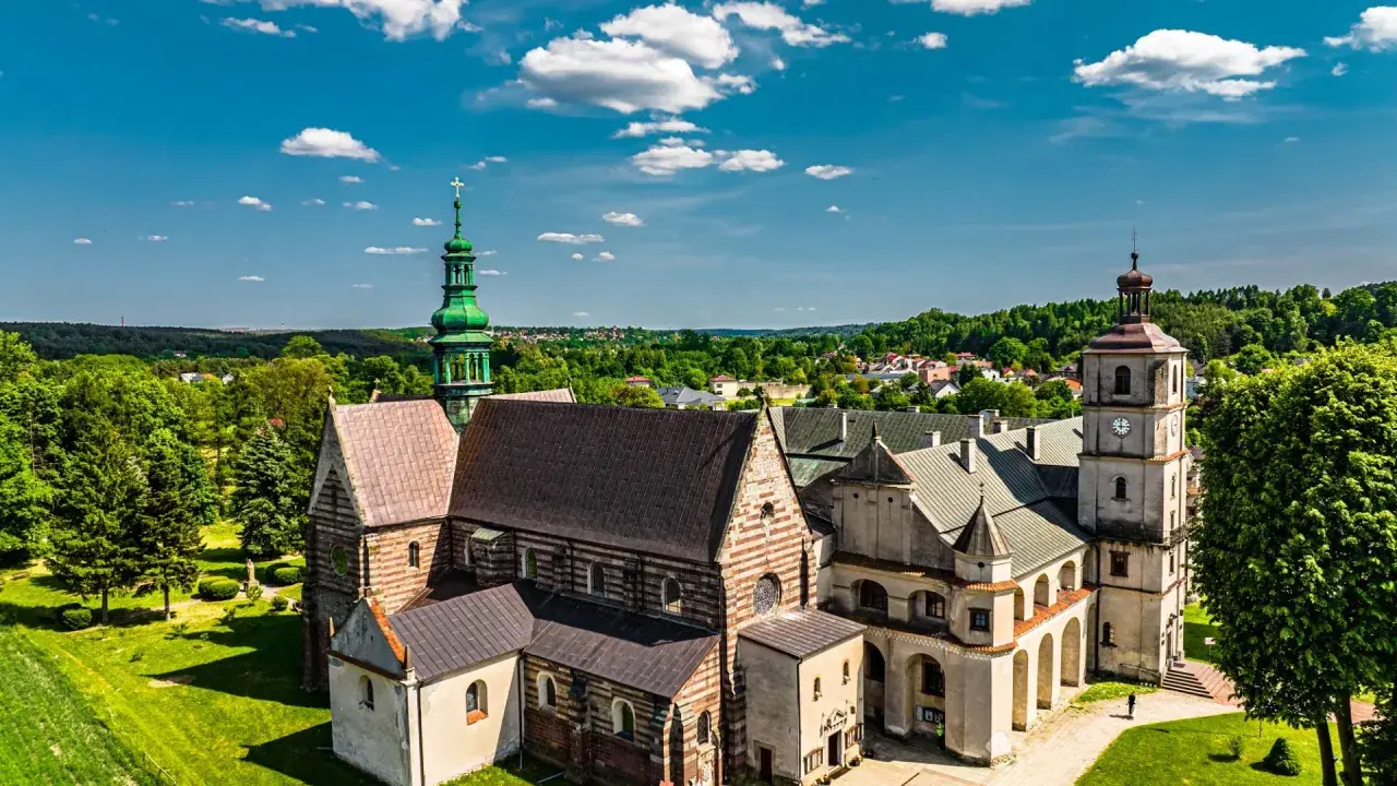 Wąchock atrakcje: Opactwo Cystersów z zieloną wieżą i wieżą zegarową na tle błękitnego nieba z chmurami.