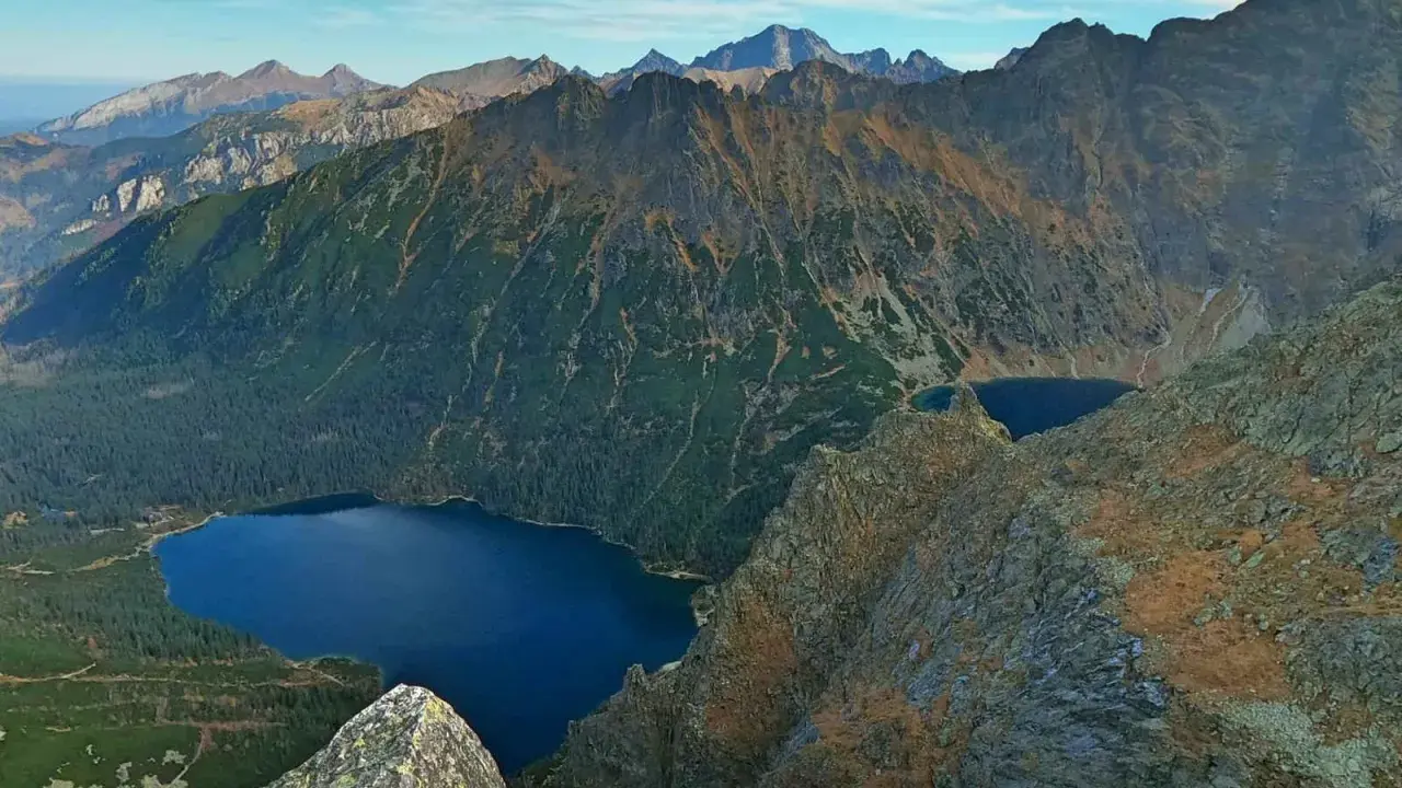 Widok na Tatry z góry. Na pierwszym planie skały, w dole las i jezioro Morskie Oko.