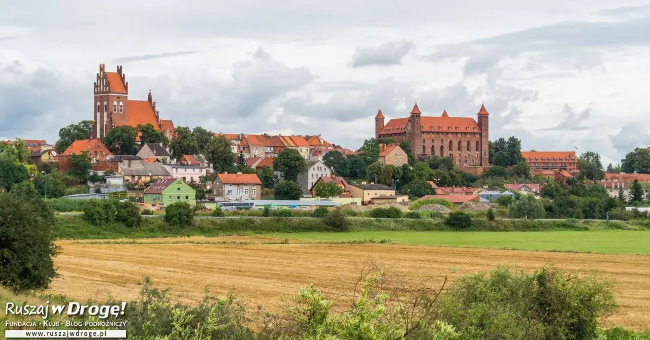 Widok na miasteczko z ceglanymi zamkami i kościołami, otoczone zielenią. W oddali pola uprawne. Wspaniałe **atrakcje** czekają na odkrycie!