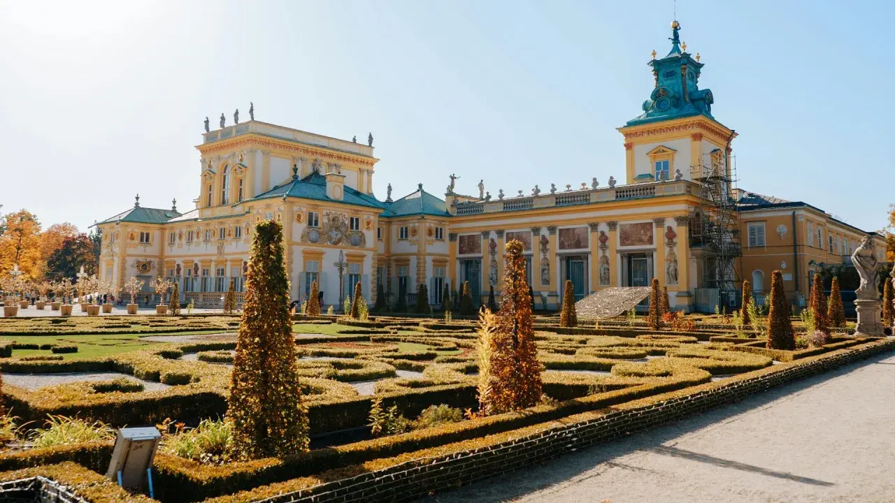 Barokowy pałac z żółtą fasadą i zielonym dachem, otoczony geometrycznym ogrodem. Wnętrze pałacu zachwyca bogactwem zdobień.