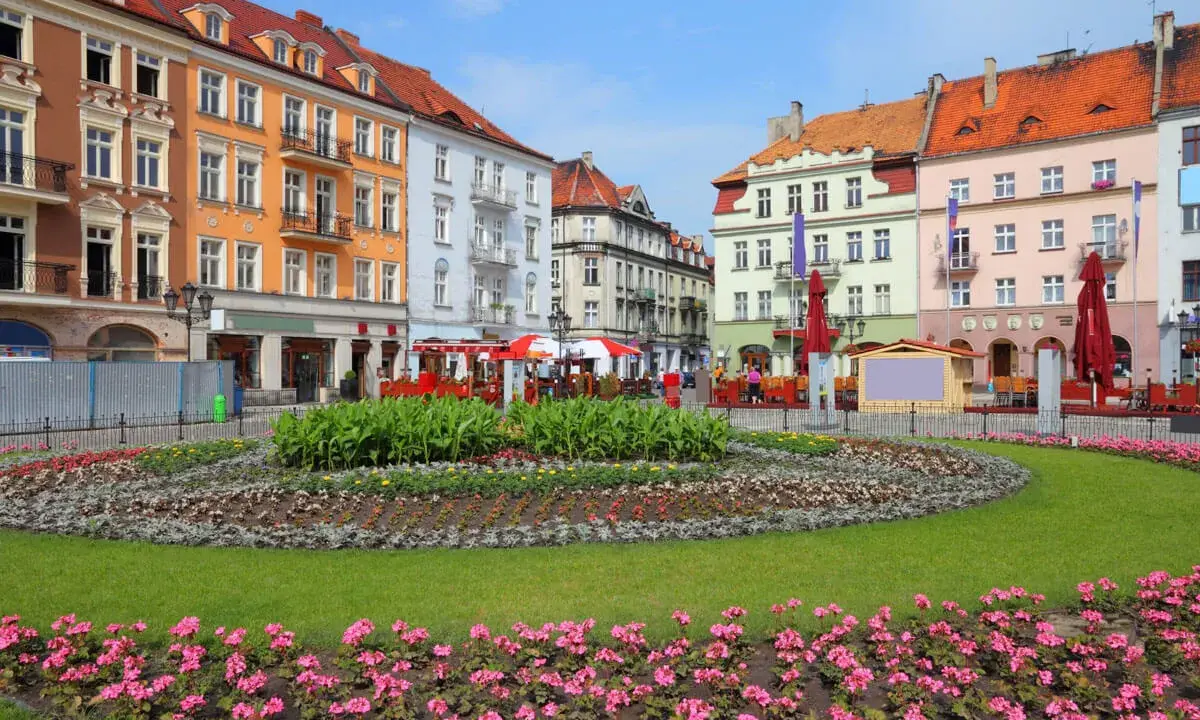 Kolorowy rynek w najstarszym mieście w Polsce, z kwitnącymi rabatami kwiatowymi i kamienicami.