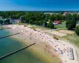 Słoneczna plaża w Giżycku tętni życiem. Ludzie odpoczywają na piasku, kąpią się w jeziorze i spacerują wzdłuż drewnianych pomostów.