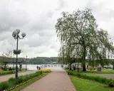 Spacer w Mrągowie nad jeziorem, z wierzbą i kwitnącymi rabatami. Idealne miejsce na relaks i podziwianie mrągowskich atrakcji.