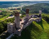 Zamek w Górach Świętokrzyskich, majestatycznie wznoszący się na wzgórzu, otoczony zielenią i malowniczym krajobrazem.