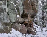 Skalna czaszka w zimowym lesie, z lodem i śniegiem na skałach i drzewach.