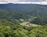 Widok z tarasu widokowego Bieszczady na zieloną dolinę z jeziorem i zabudowaniami.