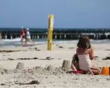 Dzieci budują zamki z piasku na plaży, w tle widać morze i falochrony. Dźwirzyno molo w oddali.