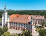 Imponujący Henryków zamek z wieżami i czerwonymi dachami, otoczony zielenią.