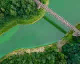 Most widoczny z lotu ptaka, przecinający zieloną wodę. Wokół bujna roślinność, tworząca malowniczą dolinę bobru.