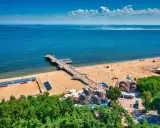 Idealne miejsce, gdzie na wakacje w sierpniu: piaszczysta plaża, molo, morze i zielone drzewa.