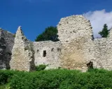 Kamienne ruiny zamku w Bydlinie, porośnięte zielenią, pod błękitnym niebem z chmurami.