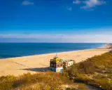 Piękna plaża i morze, idealne na spacer po urokliwych **miejscowościach nad morzem koło Gdańska**. W oddali widać charakterystyczny budynek.