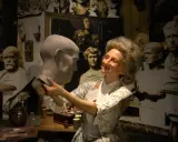 W muzeum figur woskowych artystka w historycznym stroju pracuje nad popiersiem.