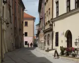 Wąska, brukowana uliczka w Lublinie z kamienicami i kilkoma spacerującymi osobami.