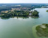 Malownicze jezioro Niesłysz z widokiem na wieś, lasy i dwa żaglówki na wodzie.