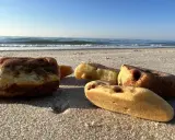 Kilka kawałków bursztynu leży na piaszczystej plaży, w tle widać spokojne morze i błękitne niebo.