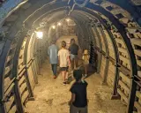Rodzina zwiedza podziemia Sandomierz, idąc przez oświetlony tunel z kamiennymi ścianami i metalowymi wzmocnieniami.