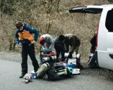 Grupa ludzi przygotowuje sprzęt do wyprawy w **Tatry Wysokie**. Widać plecaki, karimaty i torby przy białym samochodzie.