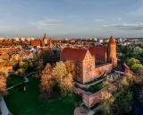 Zachód słońca nad zamkami na Mazurach. Czerwone dachy i ceglane mury w blasku złotej godziny.
