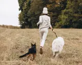 Idealne miejsce, gdzie na wakacje z psem w Polsce: kobieta biegnie z dwoma psami przez łąkę.