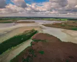 Malownicze jeziorka kozie z trzcinami i zielonymi połaciami, pod błękitnym niebem z chmurami.