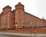 Imponujący ceglany budynek dawnego Księży Młyn, idealny na zwiedzanie. Widać znaki drogowe i ogrodzenie.