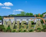Wielkie litery "WISŁA" na rynku, ozdobione błyszczącymi elementami, na tle zieleni i budynków.